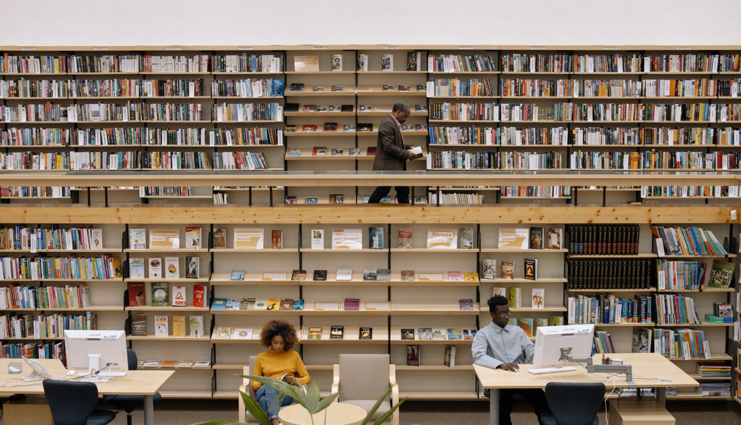 Bibliotēka ar grāmatplauktiem fonā un diviem lasītājiem priekšplānā