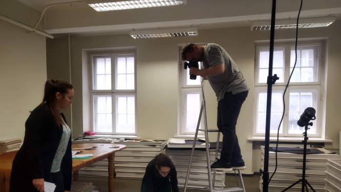 Fotogrāfs stāv uz trepēm un fotografē no augšas muzeja priekšmetu-dokumentu