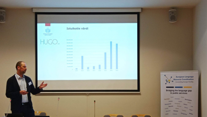 Jānis Ziediņš pie ekrāna prezentē platformas Hugo.lv izmantošanas statistiku