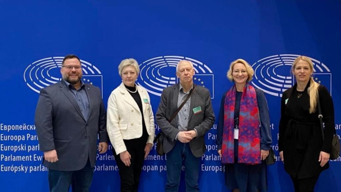 Vizītes dalībnieki stāv pie zilas sienas ar ES simboliku