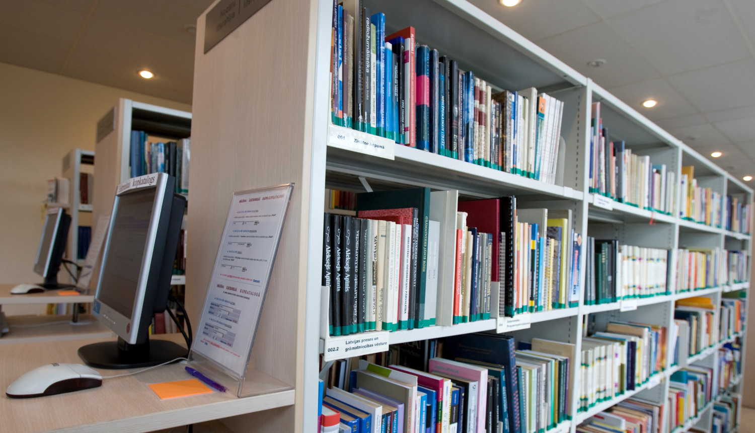 Bibliotēkas grāmatu plaukts ar datoru