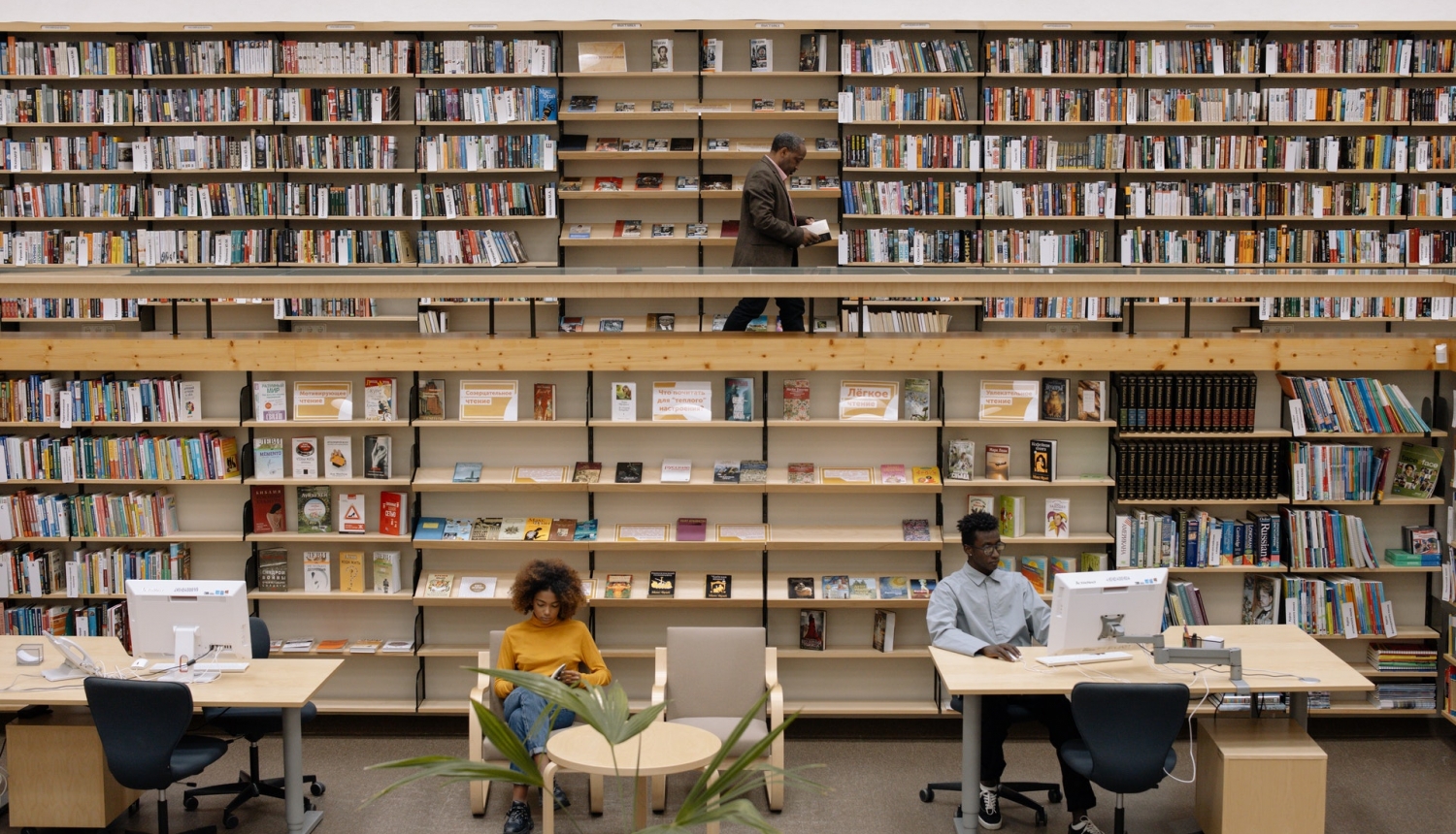Bibliotēka ar grāmatplauktiem fonā un diviem lasītājiem priekšplānā