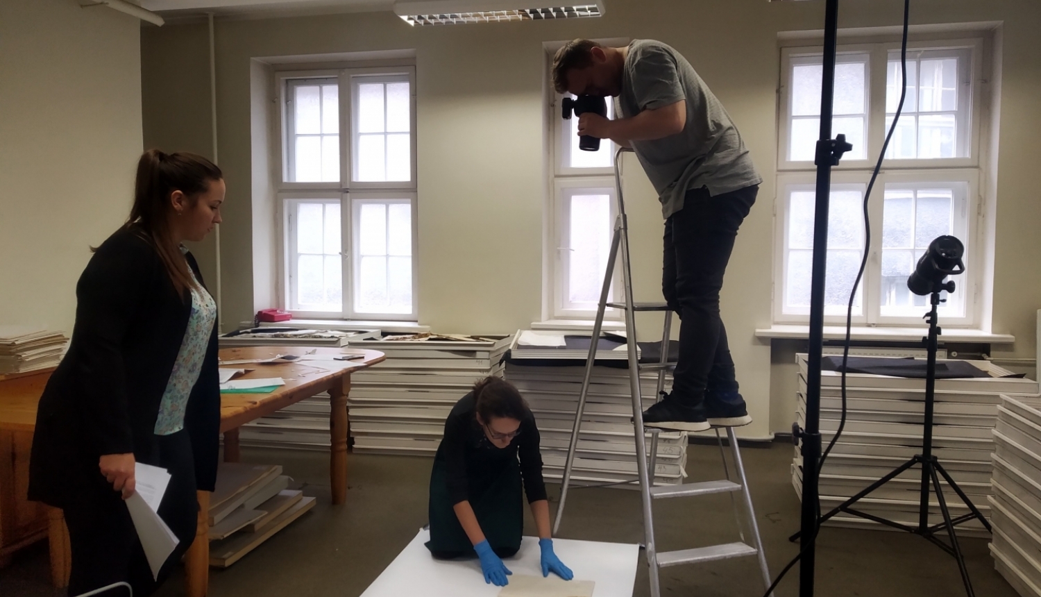 Fotogrāfs stāv uz trepēm un fotografē no augšas muzeja priekšmetu-dokumentu