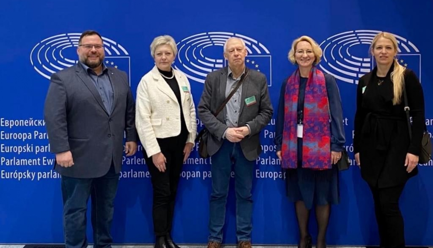 Vizītes dalībnieki stāv pie zilas sienas ar ES simboliku